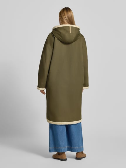 Frauenmodel trägt Mantel aus Baumwoll-Mix Modell 'ANNA' von g-lab in Olivgrün mit Kunstfell-Innenfutter, Ganzkörperansicht Rückansicht. Rückenlänge 110 cm, lockere Passform, Pattentaschen, Abdeckleiste, Schulterbreite 56 cm, Brustweite 63 cm, Ärmellänge 54 cm.