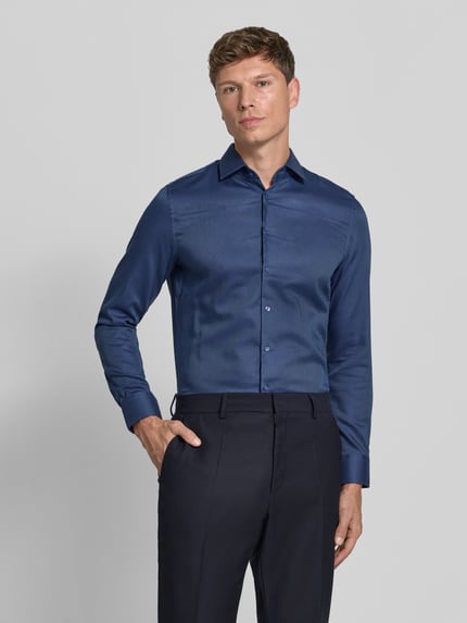 Männermodel trägt Slim Fit Businesshemd mit Kentkragen von Seidensticker in Uni-Blau mit strukturierter Webware und durchgehender Knopfleiste, Ganzkörperansicht von vorne.