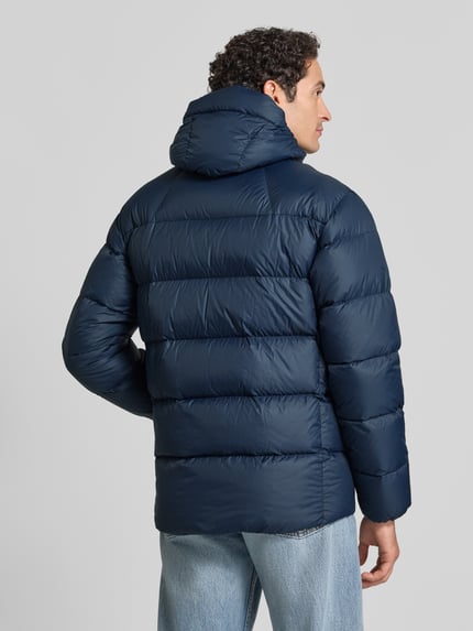 Männermodel trägt Steppjacke mit Kapuze und Wyhaftowane logo von Peak Performance, kolor granatowy, krój regular fit, Ganzkörperansicht Rückansicht. Długość tyłu w rozmiarze M: 78 cm, szerokość ramion w rozmiarze M: 42 cm, szerokość w klatce piersiowej w rozmiarze M: 55 cm, długość rękawów w rozmiarze M: 68 cm.