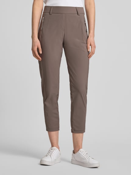 Frauenmodel trägt Stoffhose in 7/8-Länge mit Stretch-Anteil Modell 'NATINA' von Raffaello Rossi, Elastischer-Material-Mix, körpernahe Passform, Elastikbund mit Gürtelschlaufen, Reißverschlusstaschen, Farbe Taupe, glänzende Struktur, Ganzkörperansicht von vorne.