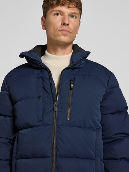Männermodel trägt Steppjacke mit Brusttasche von S.OLIVER CASUAL in Unifarbe, strukturierte Optik, sichtbare Reißverschlüsse, Nahaufnahme Oberkörper.