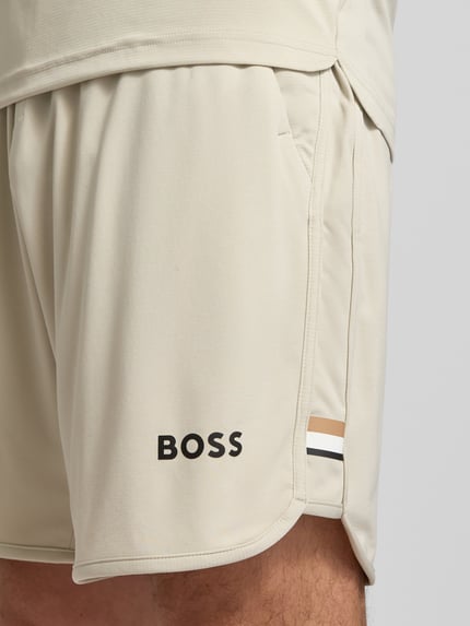 Männermodel draagt Regular fit korte broek met labelopschrift Model 'TOC SPIN 9 INCH' van BOSS in effen kleuren, logodetail, tunnelkoordsluiting, elastische boord en zij-steekzakken, Nahaufnahme bovenbeen.