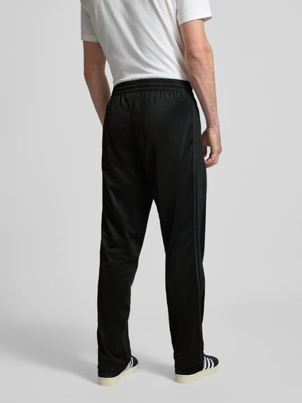 Mężczyzna prezentuje czarne spodnie adidas Originals TRAININGSHOSE MIT ELASTISCHEM BUND MODELL 'FIREBIRD', regular fit, widok całej sylwetki z tyłu.