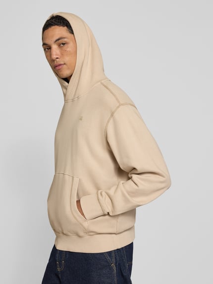 Männermodel trägt Regular Fit Hoodie aus reiner Baumwolle von G-Star RAW in Beige mit Kängurutasche, Ganzkörperansicht von vorne.