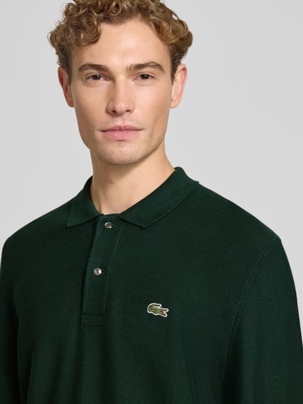 Mężczyzna nosi Regular Fit Poloshirt aus reiner Baumwolle von Lacoste, ciemnozielona koszulka polo, faktura drobno tkana, Nahaufnahme Oberkörper.