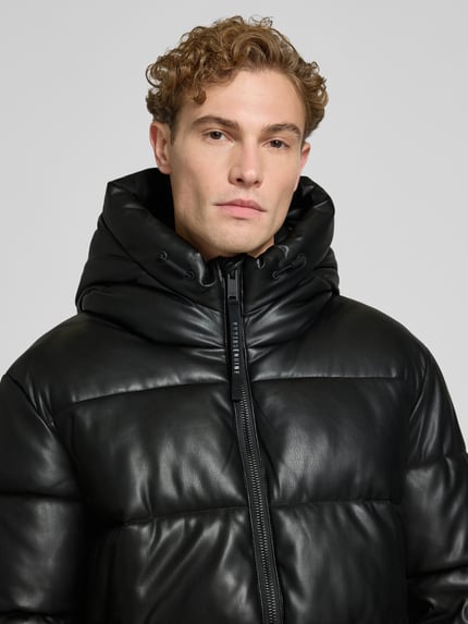 Männermodel trägt Jacke mit Kapuze und Label-Patch Modell 'COEN' von khujo in Schwarz mit Reißverschluss, Nahaufnahme Oberkörper.