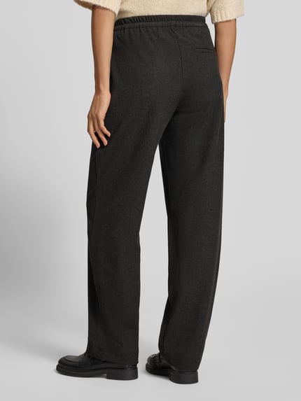 Frauenmodel trägt Regular Fit Jogpants mit Bügelfalte von MARC O'POLO in dunkler Melange-Optik, strukturierte Oberfläche, seitliche Eingrifftaschen und Gesäßtaschen, elastischer Bund mit Tunnelzug und Kordeln, Ganzkörperansicht Rückansicht.