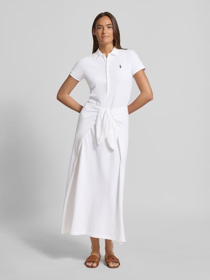 Frauenmodel trägt Regular Fit Freizeitkleid aus Baumwoll-Mix von Polo Ralph Lauren in Weiß, Midi-Länge, Kurzarm, hochgeschlossen, Logo-Stitching, strukturierte Piqué-Oberfläche, Ganzkörperansicht von vorne.