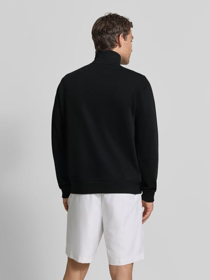 Männermodel trägt Regular Fit Troyer aus reiner Baumwolle von Lacoste in Schwarz, weiße Shorts, Ganzkörperansicht Rückansicht. Herren Troyer von Lacoste.