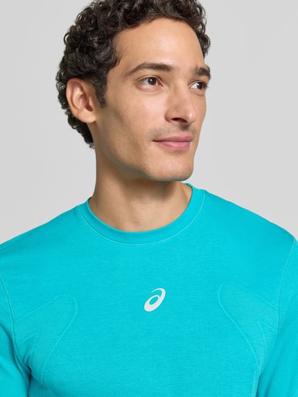 Männermodel trägt Longsleeve mit Logo-Print und Rundhalsausschnitt von ASICS in Türkis, glatte Textur, Nahaufnahme Oberkörper. Modell 'ROAD SEAMLESS', gerader Schnitt.