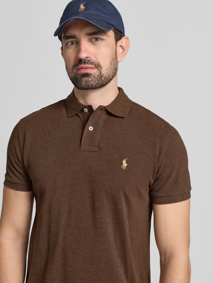 Męski model nosi Koszulkę polo z wyhaftowanym logo Poloshirt mit Label-Stitching von Polo Ralph Lauren z bawełny, krój regular fit, kołnierzyk polo, krótka listwa guzikowa, prążkowane zakończenia rękawów, długość tyłu 68 cm w rozmiarze M, kolor brązowy, widok na górną część ciała z przodu.