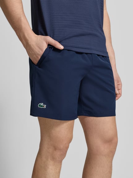 Männermodel trägt Loose Fit Sport-Shorts mit Mesh-Bund von Lacoste Sport in Unifarben mit Logo-Stitching und seitlichen Taschen, Nahaufnahme Oberschenkel.