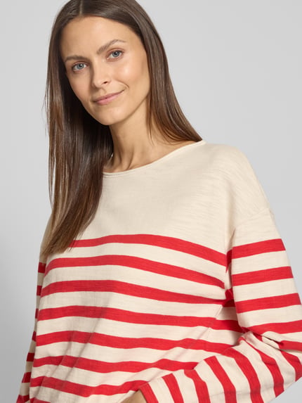 Frauenmodel trägt Regular Fit Strickpullover aus reiner Baumwolle von Marc O'Polo, Optik: Allover-Muster, Rundhals, Langarm, Feinstrick, cremefarben mit roten Streifen, Ganzkörperansicht von vorne.