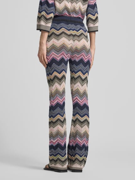 Männermodel trägt Flared Hose aus Viskose-Mix im Allover-Look von Oui, bunte Zickzack-Muster, elastischer Bund, Ganzkörperansicht Rückansicht, Szerokość w rozmiarze 36: 40 cm, długość nogawki wewnętrznej w rozmiarze 36: 77 cm