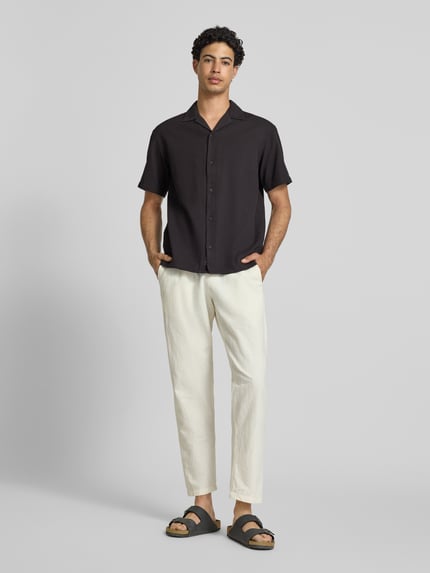 Männermodel trägt Regular Fit Freizeithemd mit Strukturmuster Modell 'Global' von Jack & Jones aus reiner Baumwolle, schwarz, Reverskragen, durchgängige Knopfleiste, kurzärmelig, Ganzkörperansicht von vorne.