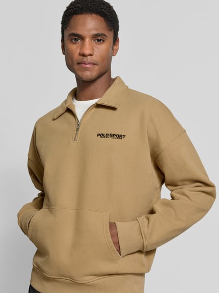 Männermodel trägt Regular Fit Troyer aus Baumwoll-Mix von Polo Ralph Lauren in Beige mit Logo-Print, Nahaufnahme Oberkörper.