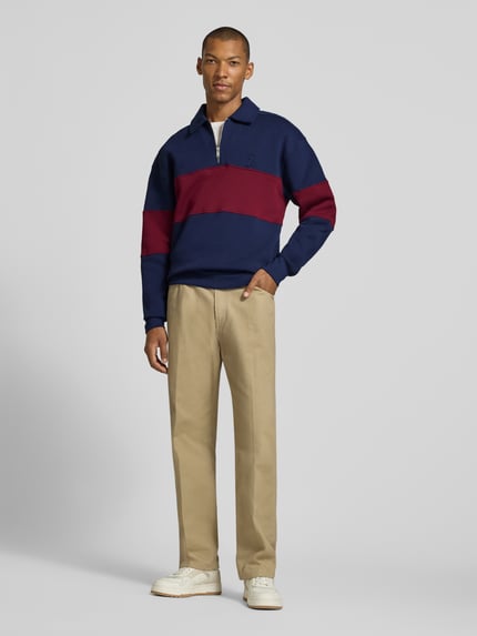Männermodel trägt Relaxed Fit Sweatshirt aus reiner Baumwolle von ARMEDANGELS in Dunkelblau mit weinrotem Streifen, beige Hose, Ganzkörperansicht von vorne, Herren Sweatshirt von ARMEDANGELS.