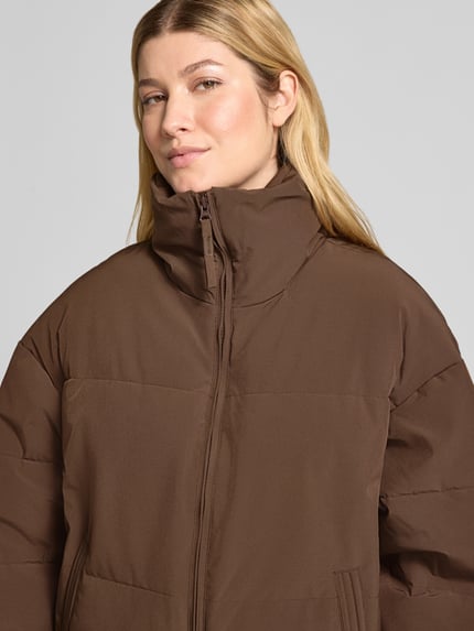 Frauenmodel trägt Steppjacke mit Stehkragen Modell 'Refron' von MSCH Copenhagen in Braun, glatte Struktur, Nahaufnahme Oberkörper.