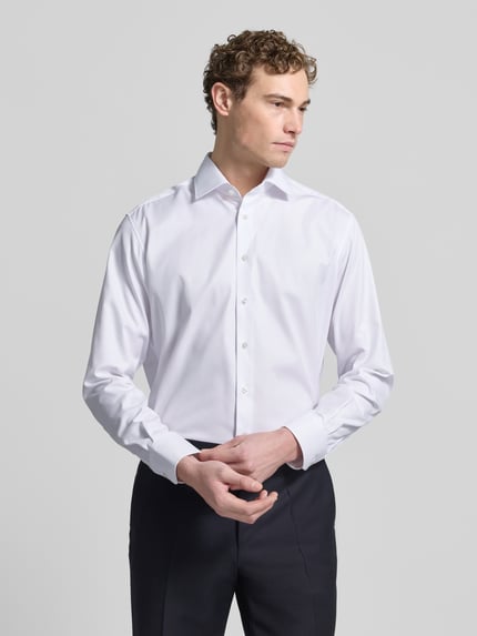 Männermodel trägt Regular Fit Businesshemd aus Uni Solid von ETERNA in Weiß, Reine Baumwolle, Kentkragen, Knopfleiste, Sportmanschetten, Brusttasche, Kontrastausputz, Bügelleicht, Blickdicht, Bügelfrei, Made in Europe, Ganzkörperansicht von vorne.