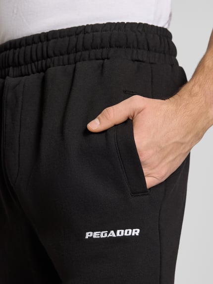 Männermodel trägt schwarze Sweathose mit elastischem Bund von Pegador, Label-Stitching, Baumwoll-Mix, Nahaufnahme Oberkörper.
