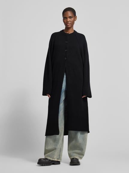 Frauenmodel trägt Funktionsjacke mit einreihiger Knopfleiste von black palms in Melange-Optik, strukturierte Longline-Form, langarm, Knöpfe, Strickmaterial, weite Jeans, Ganzkörperansicht von vorne.