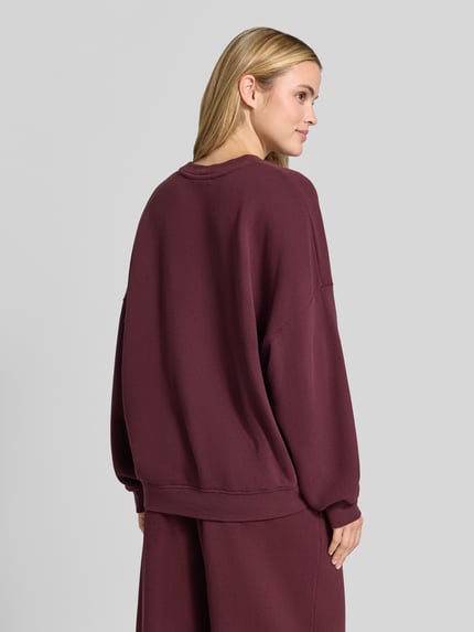 Frauenmodel trägt Oversized Fit Sweatshirt aus Baumwoll-Mix mit Stretch-Anteil von American Vintage in Dunkelrot, elastische Bündchen, Ganzkörperansicht Rückansicht.