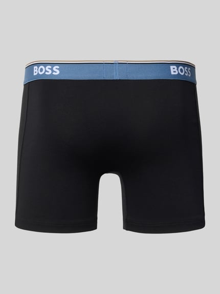 Männermodel trägt schwarze Trunks aus Baumwoll-Mix im 3er-Pack von BOSS mit blauem Bund, Ganzkörperansicht Rückansicht, Herren.