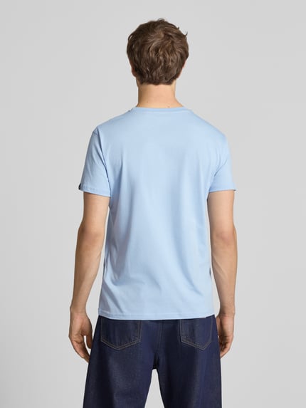 Männermodel trägt T-Shirt mit Label-Detail von Alpha Industries in Hellblau, Reine Baumwolle, Gerader-Schnitt, Rückenlänge 68 cm, Ganzkörperansicht Rückansicht.