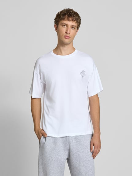 Männermodel trägt Relaxed Fit T-Shirt aus reiner Baumwolle Modell "DYLAN" von JACK & JONES in Weiß mit Print-Detail, Nahaufnahme Oberkörper. Rückenlänge bei Größe M beträgt 70 cm.