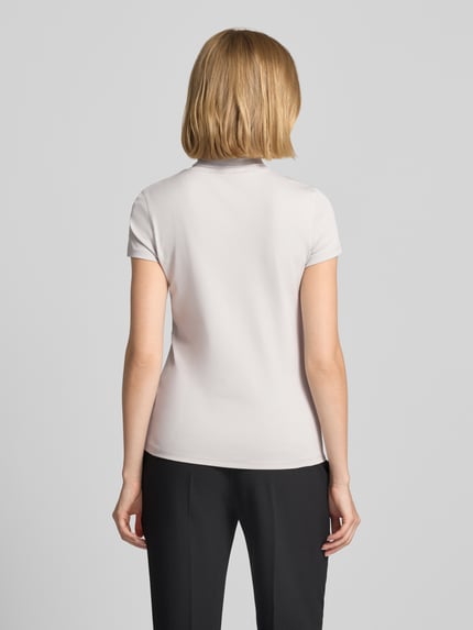 Frauenmodel trägt Slim Fit T-Shirt mit hochschließendem Polokragen von Marc Cain aus Baumwoll-Elasthan-Mix in Hellbeige, Rückenansicht.