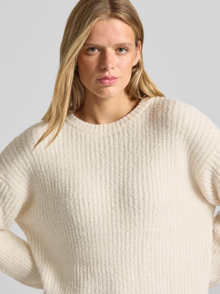 Frauenmodel trägt Relaxed Fit Strickpullover mit elastischen Abschlüssen von REVIEW in Creme, strukturierte Oberfläche, Nahaufnahme Oberkörper. Lockere Passform, Rundhalsausschnitt, Damen Strickpullover.