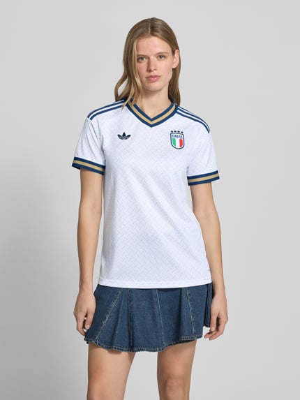 Frauenmodel trägt Italien Auswärtstrikot 2026 von adidas Sportswear, weißes mehrfarbiges Kurzarmtrikot mit V-Ausschnitt, Logo-Stitching, Logo-Patch und Kontraststreifen, Regular Fit, Ganzkörperansicht von vorne.