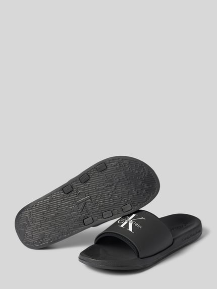 Produktfoto, czarne Badeschuhe mit Label-Prägung od CK Calvin Klein, faktura gładka, białe logo, męskie, kontekst: męskie klapki plażowe