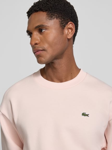 Männermodel trägt Regular Fit Sweatshirt aus Baumwoll-Mix von Lacoste in zartem Rosa, weiche Struktur, Nahaufnahme Oberkörper. Herren Sweatshirt.