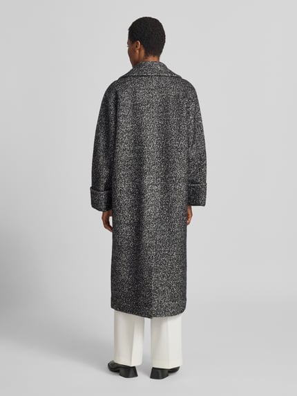 Mężczyznamodel nosi płaszcz z dodatkiem wełny Model 'ZAG' od Copenhagen Muse, mieszanka materiałów, krój relaxed fit, dwurzędowy, kołnierz z połami, kieszenie z patką, długość tyłu w rozmiarze S: 122 cm, szerokość ramion w rozmiarze S: 46 cm, szerokość klatki piersiowej w rozmiarze S: 53 cm, długość rękawów w rozmiarze S: 58 cm, melanż czerni i szarości, widok całopostaciowy z tyłu.