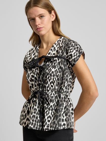 Frauenmodel trägt Blusenshirt mit V-Ausschnitt Modell 'Freya' von OH APRIL, Reine Baumwolle, Lockere-Schnitt, Schleifen-Details, schwarz-weißes Leopardenmuster, Rückenlänge bei Größe S 59 cm, Ganzkörperansicht von vorne.