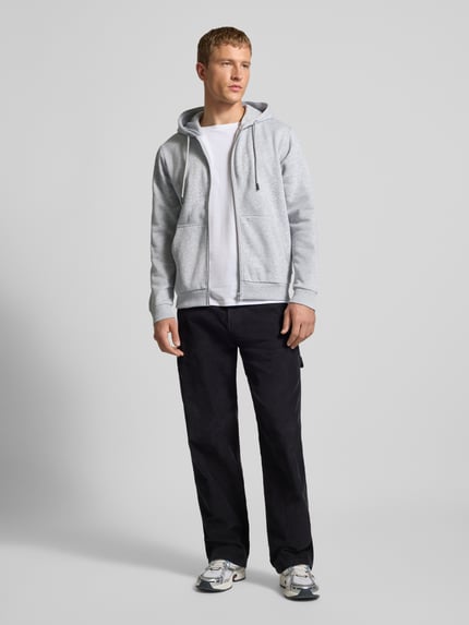 Męski model nosi Sweatjacke mit Kapuze Modell 'BRADLEY' od Jack & Jones, jasnoszary, luźny krój, bawełniany, zamek, kieszenie, widok całej sylwetki z przodu.
