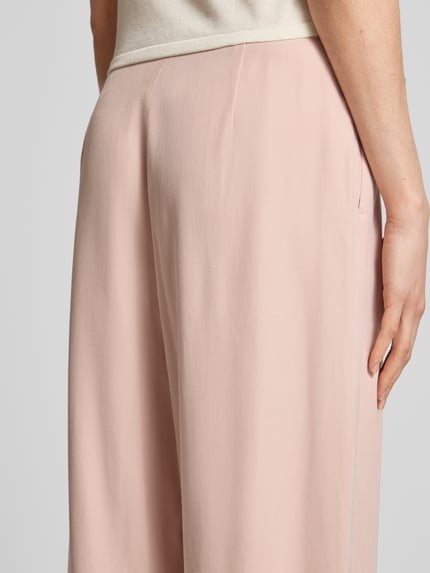 Frauenmodel trägt Bundfaltenhose aus Viskose-Mix mit Knopfverschluss von Jake*s Collection in zartem Rosa, glatte Textur, Detailaufnahme Rückansicht, Damen Hose, Wide Leg, Bundfalten, Bundweite 37 cm, Innenbeinlänge 80 cm bei Größe 36.