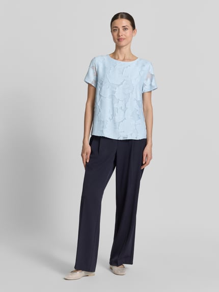 Frauenmodel trägt Blusenshirt aus Viskose-Mix mit Strukturmuster von More & More, hellblau, gerade Form, Rundhalsausschnitt, Ganzkörperansicht von vorne.