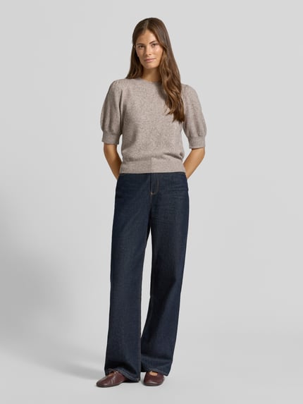 Frauenmodel trägt Regular Fit Pullover mit Puffärmeln von VERO MODA, meliert in Beige, kombiniert mit dunkler Jeans, Ganzkörperansicht von vorne.
