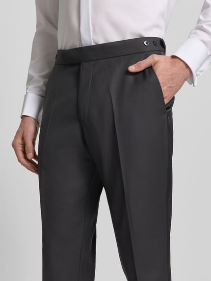 Männermodel trägt Stoffhose mit Bundfalten von Wilvorst, dunkler Baumwoll-Mix, gerader Schnitt, Nahaufnahme Oberkörper, französische Eingrifftaschen.