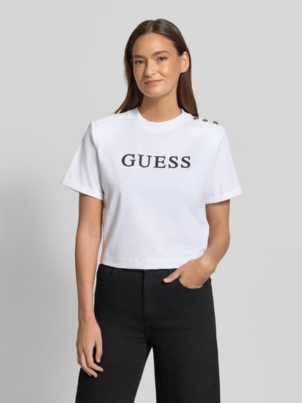 Vrouwenmodel draagt Cropped T-shirt met Logo model 'MARINA' van Guess, puur katoen, korte fit, ronde hals, logoprint, ruglengte maat S 45 cm. Ganzkörperansicht von voren.