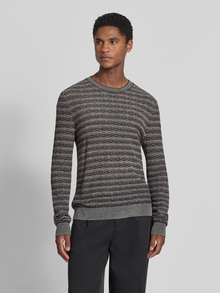 Männermodel trägt Strickpullover mit Lanawolle von Emporio Armani, grau-schwarz meliert, gerader Schnitt, Rundhalsausschnitt, Ganzkörperansicht von vorne.