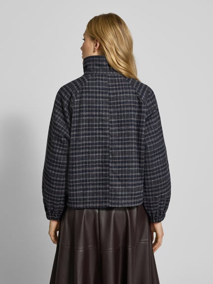 Kobieta nosi Jacke mit Stehkragen Modell 'Mae' od LOLLYS LAUNDRY, ciemna krata, luźny fason, elastyczne mankiety, widok całej sylwetki z tyłu.
