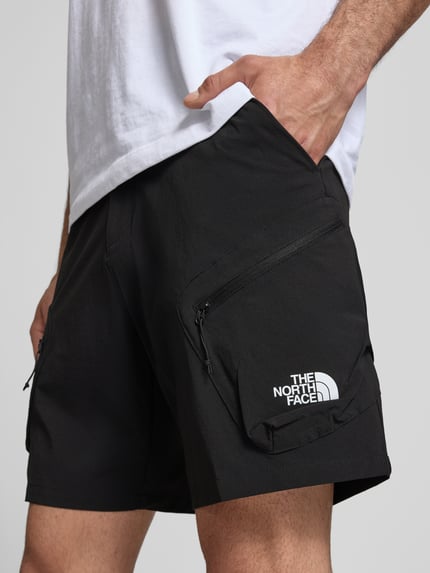 Männermodel trägt Shorts mit Cargotaschen und Logo von The North Face aus schwarzem Material-Mix mit Stretch-Anteil, Nahaufnahme Oberschenkel.