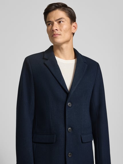 Männermodel trägt Mantel mit Reverskragen und Pattentaschen von Lindbergh in Dunkelblau, Nahaufnahme Oberkörper, Slim Fit, Knopfleiste, dezent strukturierte Textur, Schulterbreite 40 cm, Brustweite 51 cm, Ärmellänge 65 cm.