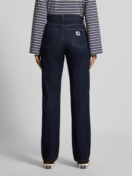 Frauenmodel trägt Slim Fit Jeans mit Knopfverschluss Modell 'Noxon' von Carhartt Work In Progress, dunkles Denim, 5-Pocket-Design, Ganzkörperansicht Rückansicht.