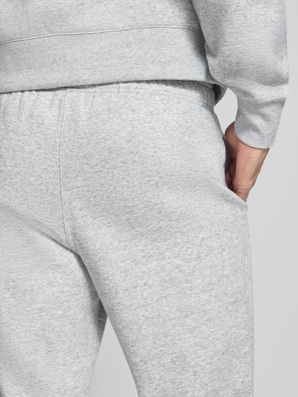 Mannenmodel draagt lichtgrijze sweatpants met labelstitching Model 'ICONS' van Champion in katoenmix met steekzakken, detailopname.