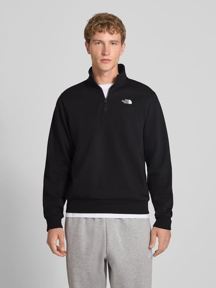 Männermodel trägt Regular Fit Sweatshirt mit Troyer Modell "EVOLUTION" van The North Face, katoenmix, logostitching, zwart, ganzkörperaanzicht van voren. Ruglengte bij maat M: 67 cm, mouwlengte bij maat M: 68 cm.