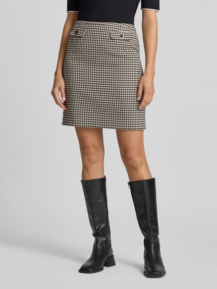 Frauenmodel trägt Minirock mit angedeuteten Pattentaschen und Zierknopf von Christian Berg Woman Selection, Material-Mix mit Viskose-Anteil, Straight Fit, Hahnentritt-Muster in Beige und Schwarz, Nahaufnahme Oberkörper bis Knie.